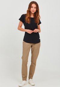 T-shirt marine à manches courtes en coton, associé à un pantalon beige coupe droite et des baskets blanches, avec un accent logo subtil sur le t-shirt.