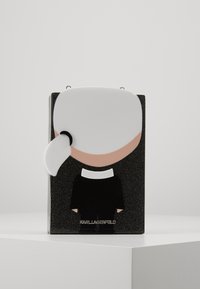 Black and white figurine with a glossy finish, featuring a stylized head, ponytail, and a black outfit, with the brand name "KARL LAGERFELD" at the base.