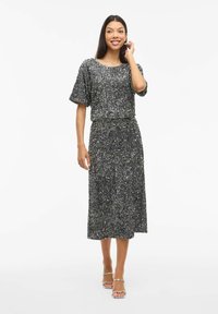 Vestido gris brillante de lentejuelas con mangas cortas, a la altura de la rodilla, con cintura elástica y un ajuste relajado, combinado con sandalias plateadas de tiras.