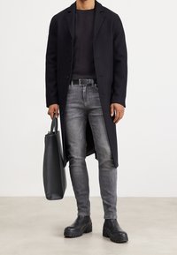 Cappotto di lana nero, jeans grigi aderenti, stivali di pelle nera con suole testurizzate e una borsa a tracolla nera. Design semplice e moderno con una palette di colori neutri.