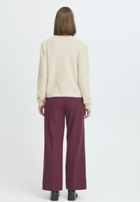 Maglione di colore crema, texture, abbinato a pantaloni larghi bordeaux con risvolti e stivaletti neri alla caviglia. Vista posteriore dell'outfit.