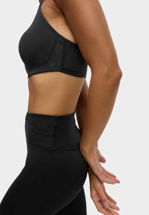 Zwarte sportbh met een asymmetrisch ontwerp. Beschikt over een zachte stof en naadloze randen. Hoogsnap zwarte leggings met stikseldetails.
