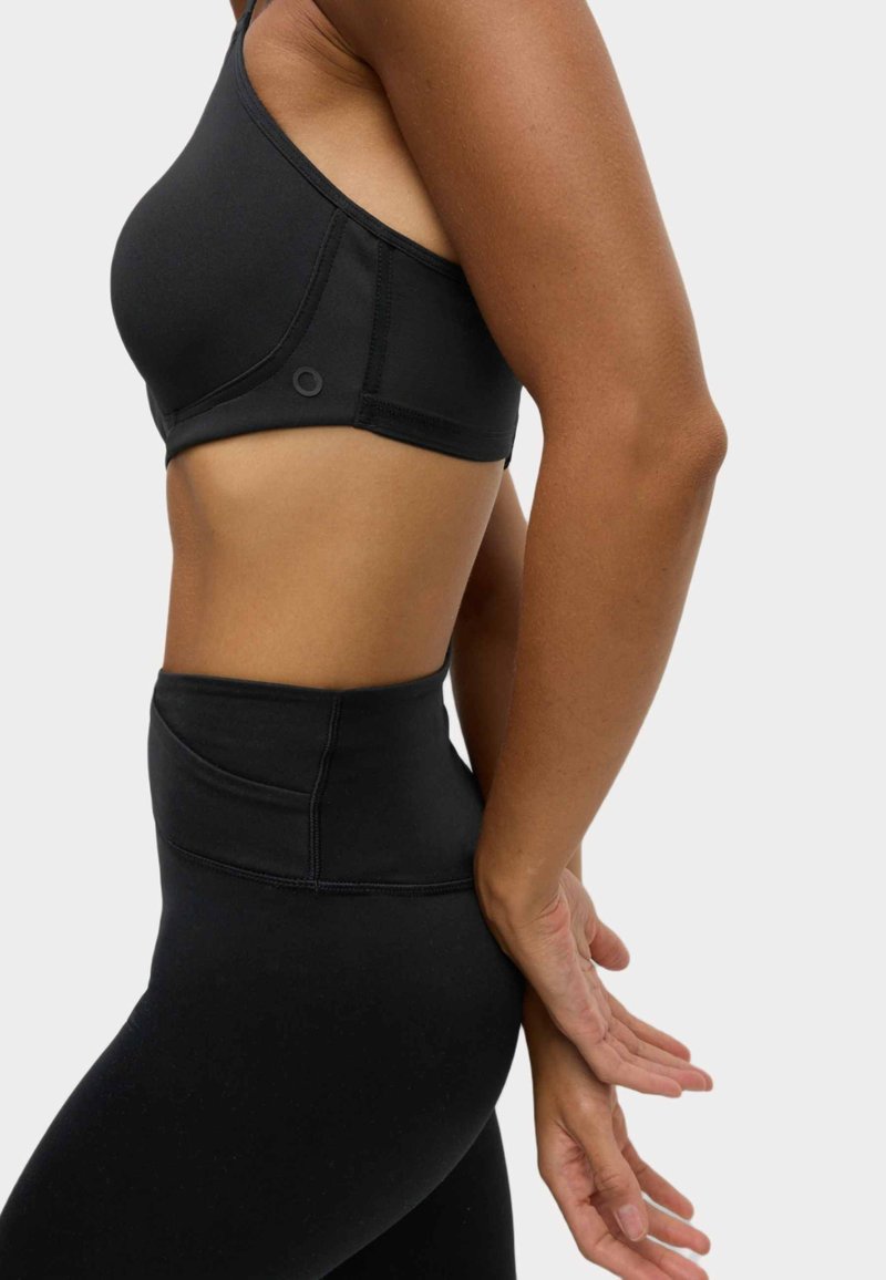 Svart sport-bh med enaxel-design. Har slät tyg och sömlösa kanter. Högmidjade svarta leggings med sömnadsdetaljer.