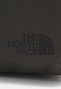 Pochette en tissu noir avec un motif en grille, arborant le logo noir bien visible de "THE NORTH FACE". Texture lisse avec des coutures renforcées.