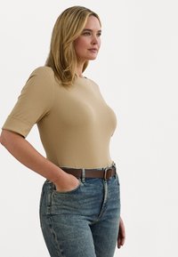 Body nude cu mânecă scurtă, cu un design ajustat, asortat cu blugi din denim albastru cu talie înaltă și o curea maro. Textură netedă, fără modele.