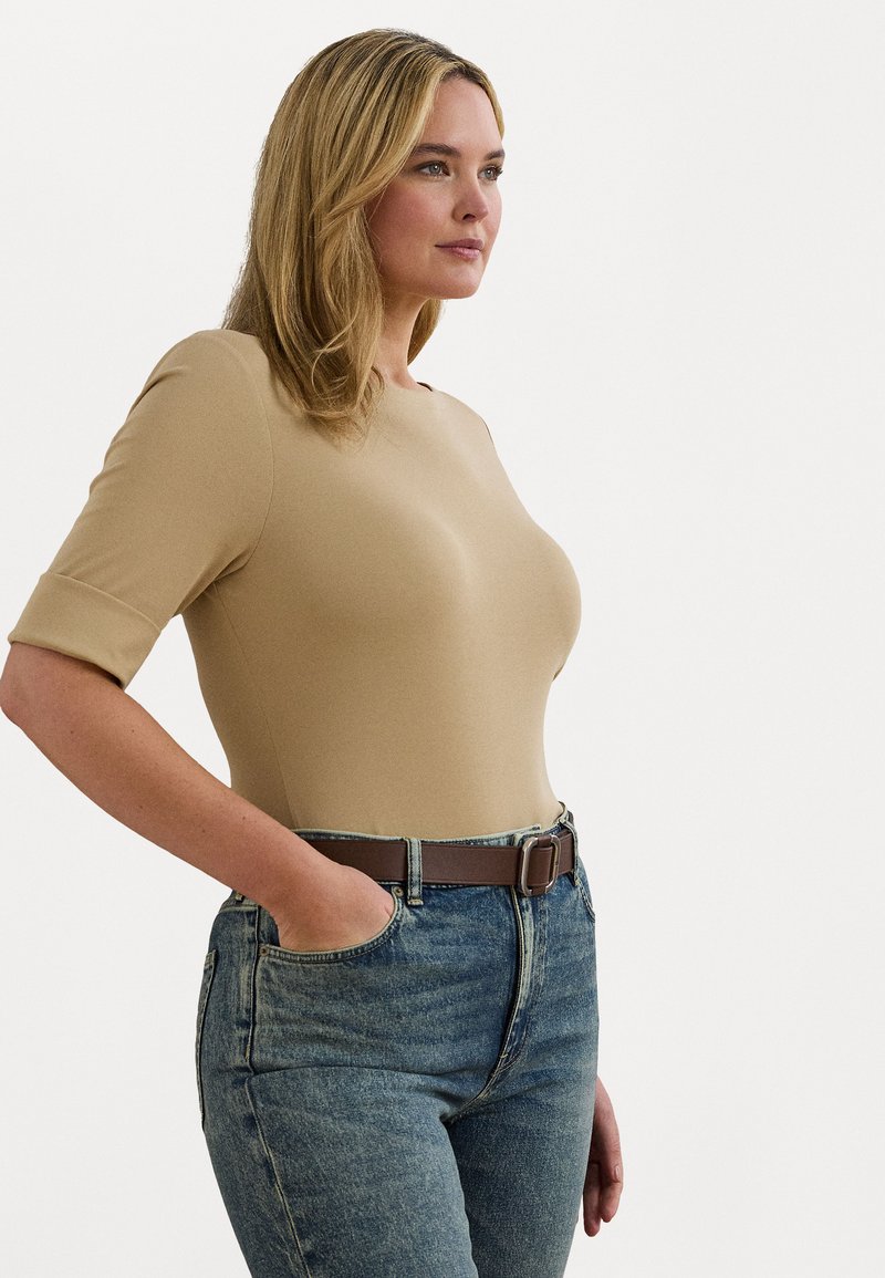 Body nude cu mânecă scurtă, cu un design ajustat, asortat cu blugi din denim albastru cu talie înaltă și o curea maro. Textură netedă, fără modele.