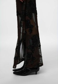 Robe noire en organza brodée de fleurs, avec une fente latérale, associée à des escarpins pointus en cuir verni noir à texture crocodile.