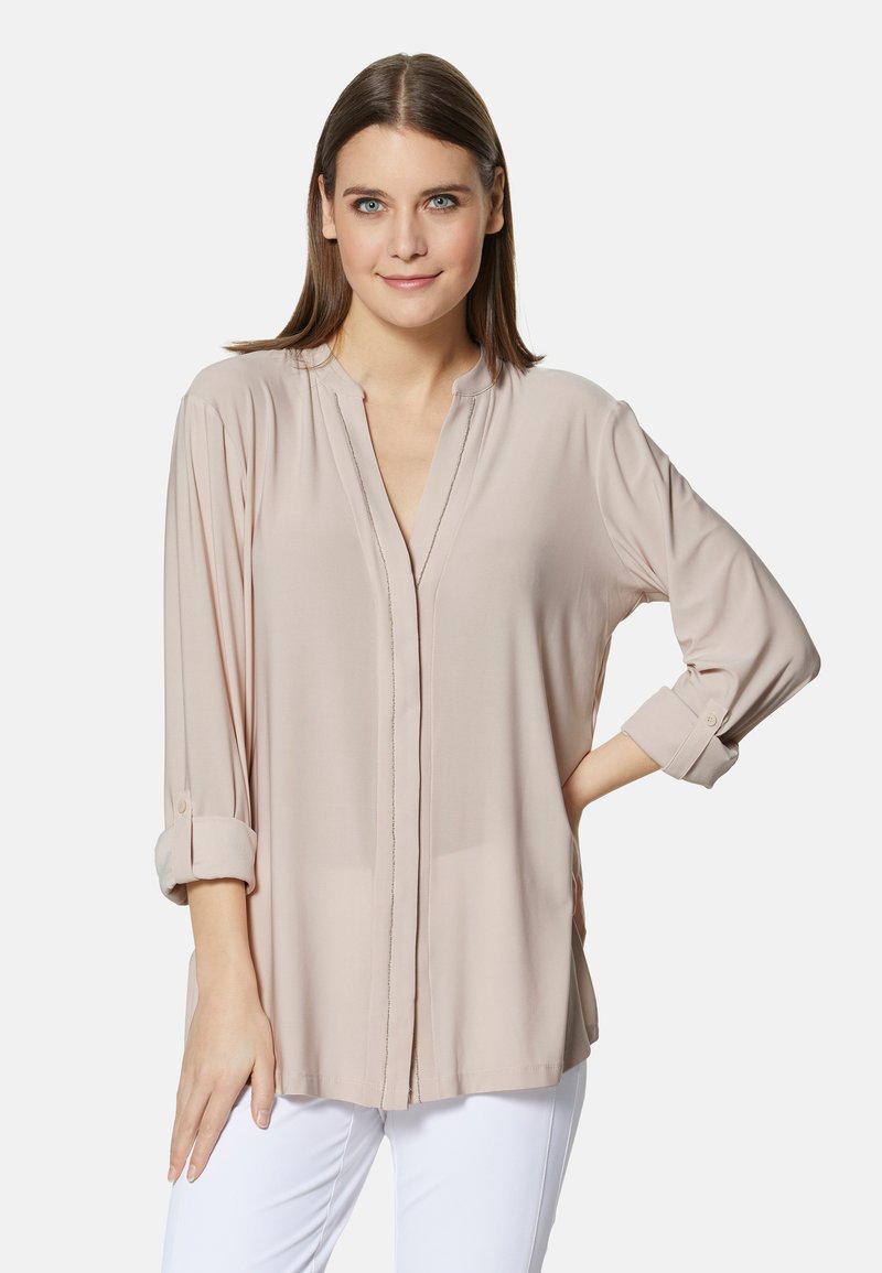 Helle beige Bluse mit langen Ärmeln, V-Ausschnitt, hochgerollten Bündchen und einem feinen Nahtdetail vorne. Hergestellt aus weichem, glattem Stoff.