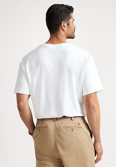 Vit bomullst-shirt med korta ärmar, rund halsringning och lös passform, kombinerad med ljusbruna byxor med bakfickor och logotypdetalj.