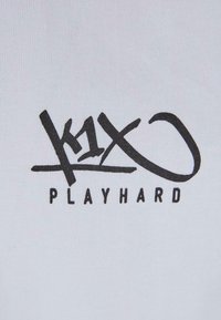 White cotton fabric featuring black graphic text, "k1X" with a stylized "X" and the word "PLAYHARD" below. Smooth texture, casual design.
