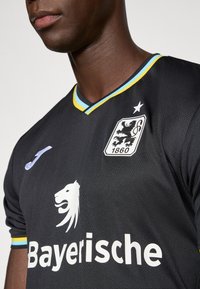 Juoda sportinė apranga su mėlynomis ir geltonomis detalėmis, su balto liūto grafika, užrašu „Bayerische“ ir skydelio logotipu su liūtu.