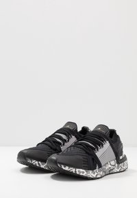 Zapatillas deportivas negras con una parte superior de tela texturizada, diseño a rayas, cordones negros y una suela blanca con estampado de serpiente.