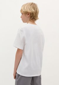 T-shirt bianca in cotone con maniche corte e collo rotondo, vista da dietro. Tessuto morbido, vestibilità rilassata, senza loghi o grafiche visibili.