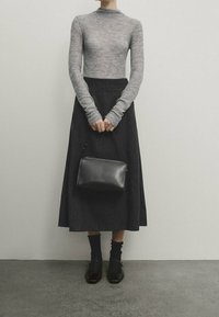 Maglietta grigia a maniche lunghe, gonna nera a trapezio, borsa nera, calze nere e scarpe con tacco a blocco. Dettagli in maglia testurizzata e pelle liscia.