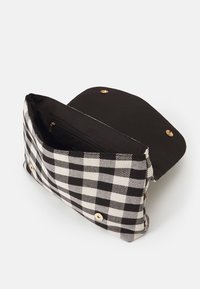 Sort-hvid ternet clutchtaske med sort stofindvendig, magnetlås, og indvendig lynlåslomme, vist åben på en hvid baggrund.