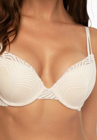 Helle beigefarbene BH mit Spitze, glatten Formcups und dünnen verstellbaren Trägern, die am Saum ein geometrisches Muster aufweisen.