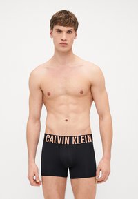 Calvin Klein schwarze Boxer Shorts mit einem weichen, elastischen Bund, auf dem der Markenname in Pink aufgedruckt ist. Glatter Stoff mit körpernaher Passform.