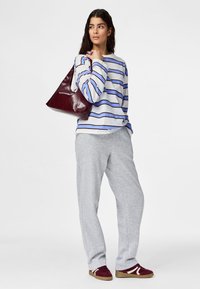 Woman wearing a striped long-sleeve shirt, gray sweatpants, and burgundy sneakers, holding a large burgundy leather handbag over her shoulder.