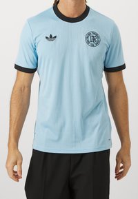 Ljusblå polyester T-shirt med svart ribbad krage och ärmslut, med vertikala ränder och en rund logotyp på bröstet.