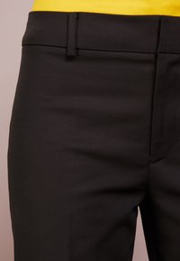Černé kalhoty s hladkým povrchem, vybavené plochým pasem a úzkým střihem. Jsou kombinovány se žlutým topem.