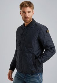 Navy gesteppte Jacke mit Stehkragen, Druckknöpfen und zwei Seitentaschen. Verfügt über ein strukturiertes Design und ein Markenlabel am linken Ärmel.