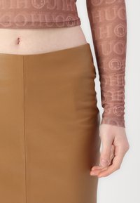 Rosemønstret, tettsittende langermet topp i gjennomsiktig stoff, kombinert med et høyt liv, glatt brun faux lærsnor.