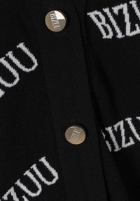 Zwarte gebreide stof met witte herhaalde "BIZUU" tekst en twee ronde metalen knopen, eveneens gegraveerd met de tekst "BIZUU".