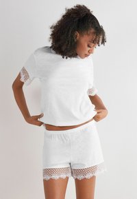 Witte loungewear set met een top met korte mouwen en kantaccenten, en bijpassende shorts met kantafwerking aan de onderzijde. Zachte, lichtgewicht stof.