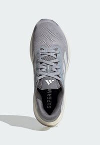 Baskets de sport grises avec une tige en maille respirante, des lacets plats, un col rembourré et des accents blancs sur la semelle et le logo. Design texturé.