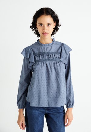 Light blue top with ruffled sleeves, textured polka dot pattern, and gathered accents at the chest and collar. Long sleeves with elastic cuffs.