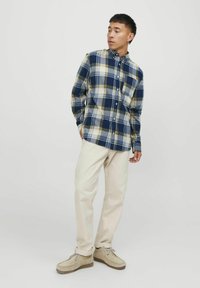 Camisa de cuadros en azul marino, beige y azul claro; combinada con pantalones color crema y zapatos de ante color beige.