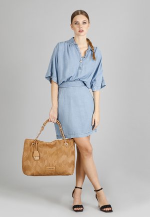 Abito camicia in denim con vita arricciata, abbinato a una grande borsa in pelle beige con manici a catena e dettagli del marchio.