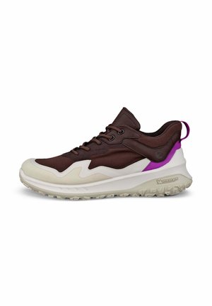 Bruine en crème sneaker met een textuur bovenwerk, contrasterende paarse accenten en een stevige witte zool met een grippatroon.