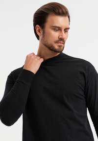 Svart långärmad tröja med rund hals, tillverkad av mjukt tyg, med en figursydd design och subtila sömdetaljer på ärmarna.