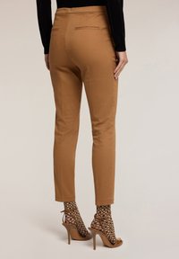 Tan broek met een gladde textuur en slim fit, met een achterzak en zijnaad, gecombineerd met hoge hakken en gestreepte sokken.