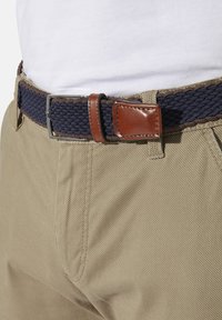 Navy woven belt with brown leather accents, secured with a silver metal buckle, worn over tan fabric trousers. Close-up view.