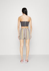 Top senza spalline in denim nero con chiusura a zip, abbinato a pantaloni corti a righe pastello. La modella indossa sandali con tacco rosa.