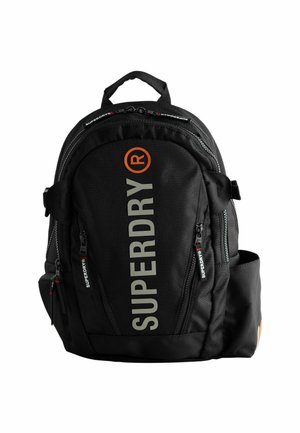 Črna nahrbtnik s velikim napisom "SUPERDRY" v sivi in oranžni barvi, več zadrgami in oblazinjenimi naramnicami. Trajna material.