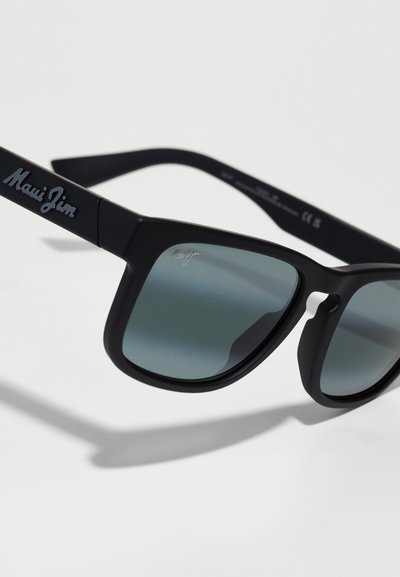 Svarta Maui Jim-solglasögon med grå gradientlinser, kantig design och framträdande logotyp på skalmen. Slät matt yta.