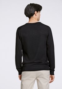 Schwarzer Strickpullover mit langen Ärmeln, gerippten Bündchen und Saumdetails, mit Rundhalsausschnitt und glatter Textur. Von hinten getragen dargestellt.