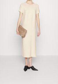 Abito maxi beige a maniche corte realizzato in tessuto liscio, abbinato a una pochette taupe texturizzata e a delle mules nere a punta.