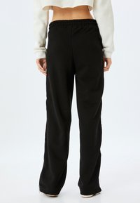 Schwarze Sweatpants mit lockerer Passform, elastischem Taillenbund und seitlichen Reißverschlüssen am Saum. Glatte Stofftextur, keine sichtbaren Muster.
