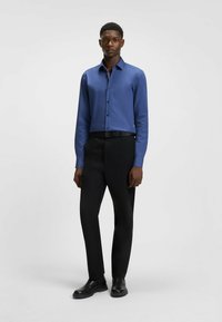 Camicia blu con bottoni in tessuto liscio, abbinata a pantaloni neri su misura e stivaletti neri, con una vestibilità slim e un design moderno.