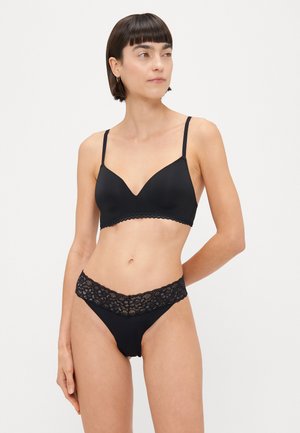 Schwarzes Dessous-Set bestehend aus einem nahtlosen Bralette mit tiefem Ausschnitt und einem passenden String mit Spitzenbund.