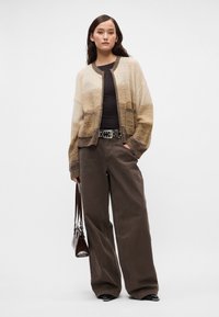 Πλέκτο κασκόλ σε μπεζ και καφέ αποχρώσεις, φαρδιές μανσέτες, ριμπ μανίκια, συνδυασμένο με ψηλόμεσα καφέ παντελόνια και μια σκούρα δερμάτινη τσάντα.