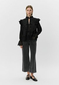 Blusa negra con mangas con volantes y detalles recortados, combinada con culottes de mezclilla negra de talle alto y zapatos planos negros.