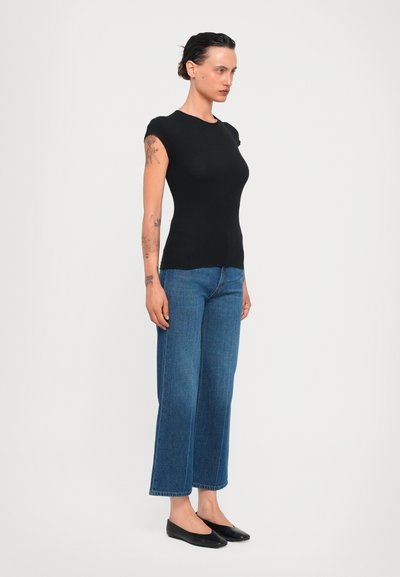 Svart tajt topp med korta ärmar, kombinerad med högmidjade, vida blå jeans och svarta platta skor. Enkelt och strömlinjeformat design.