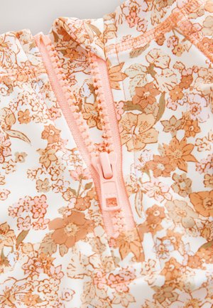 Tela con estampado floral en colores pastel que presenta tonos durazno y beige. Cierre de cremallera en plástico color durazno a juego con costuras visibles.