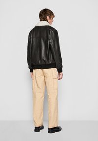 Black leather jacket with a white shearling collar, paired with light beige cargo pants featuring pockets and pink stitching. Black shoes.