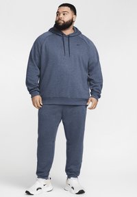 Sudadera navy blue y pantalones de chándal a juego, hechos de tejido suave, con capucha ajustable, puños acanalados y zapatillas blancas con acentos negros.